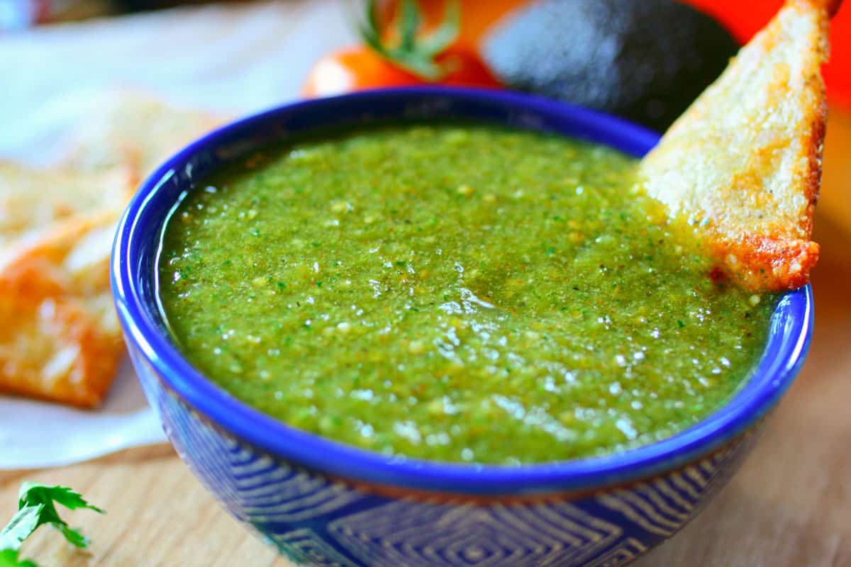 Green chili salsa with tomatillo in a blue bowl with a white pattern and a side of keto chips.