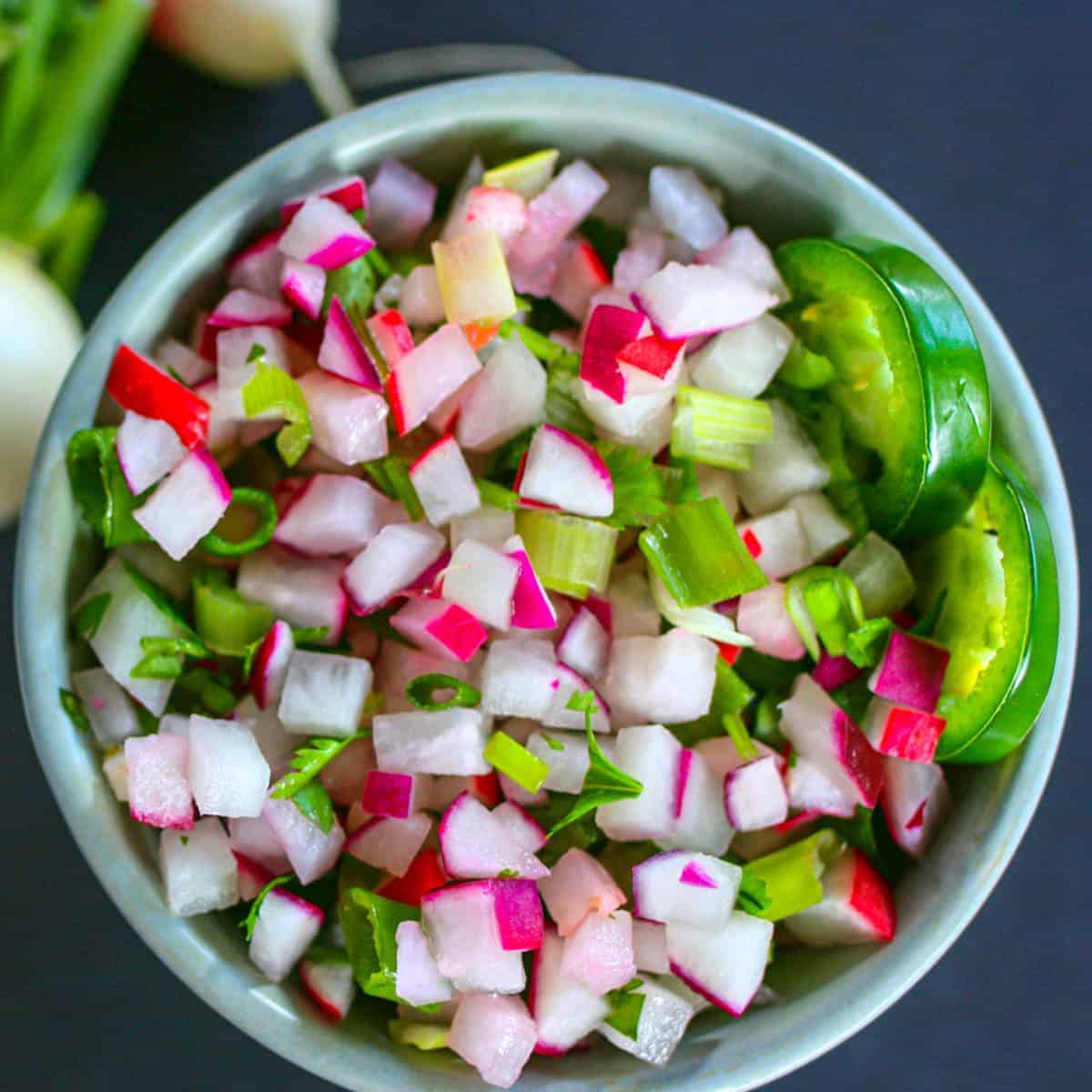 Radish salsa and jalapeno slices in a grey bowl with a dark grey background.
