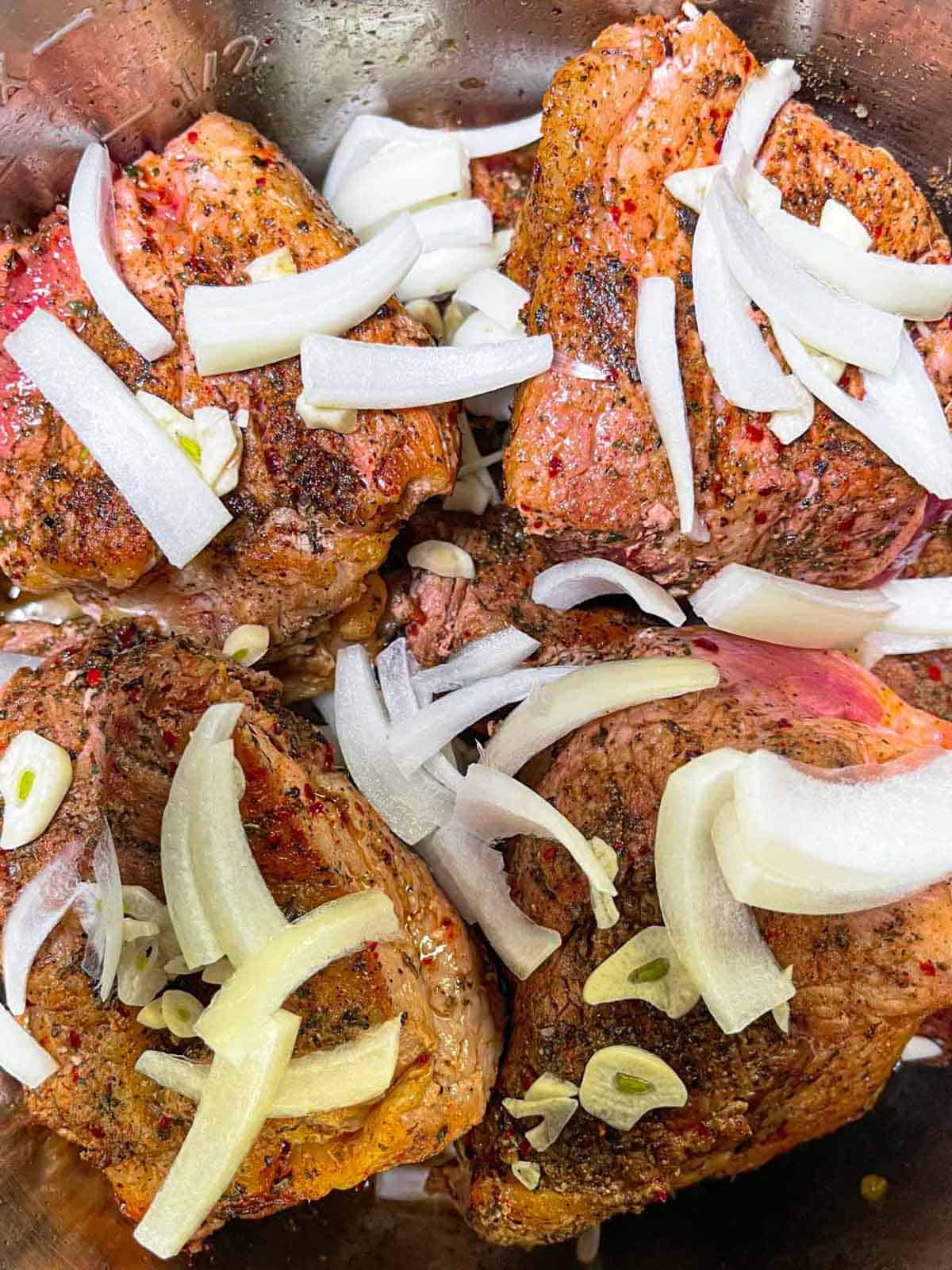 Seared pork chunks in Instant Pot with raw onion and garlic slices ready to cook.