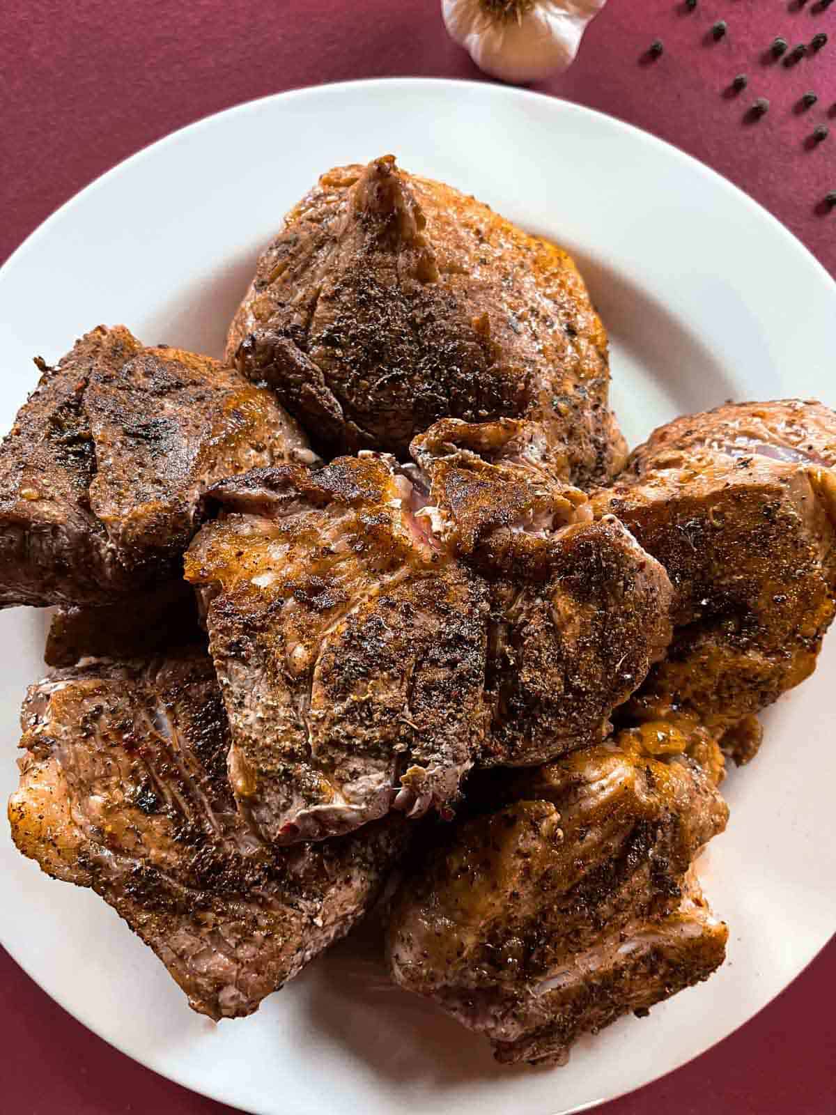 Seared pork chunks piled on a white plate sitting on a brick red background.