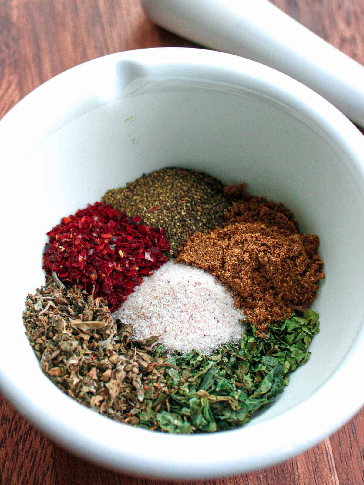 Colorful piles of rub spices in a white mortar and pestle.