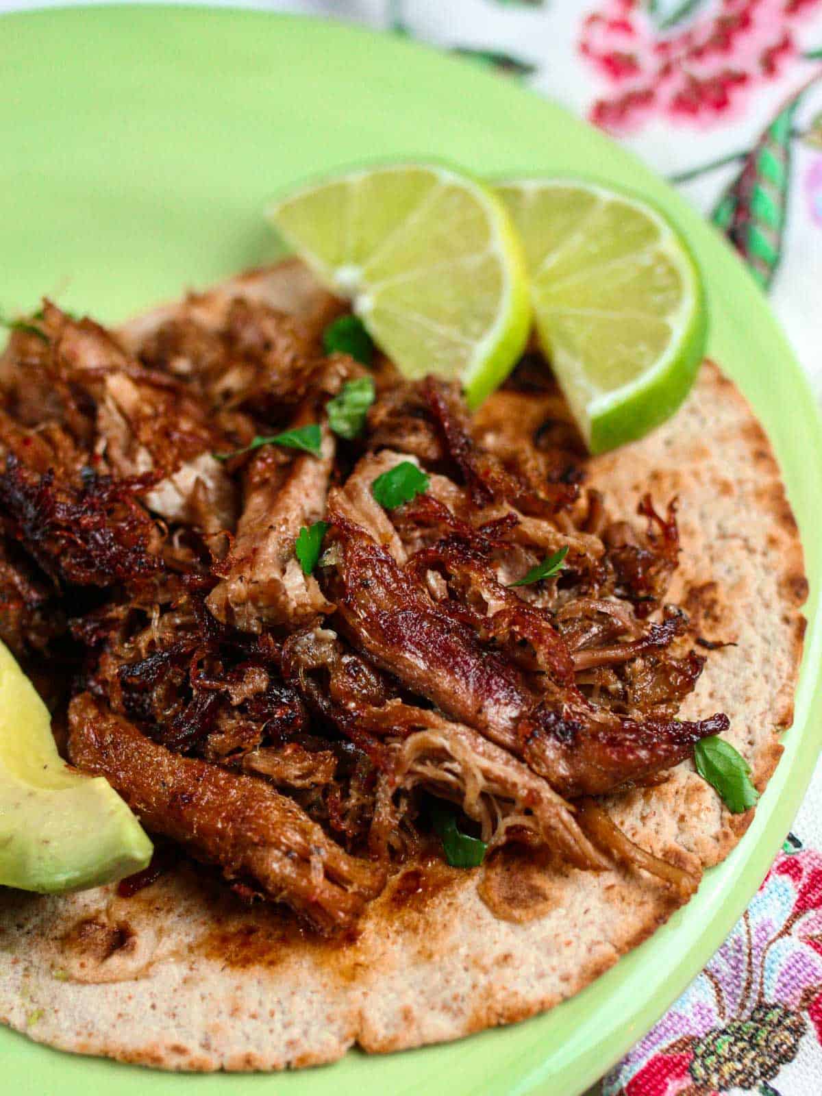 Keto carnitas taco with a side of lime and avocado on a green plate.