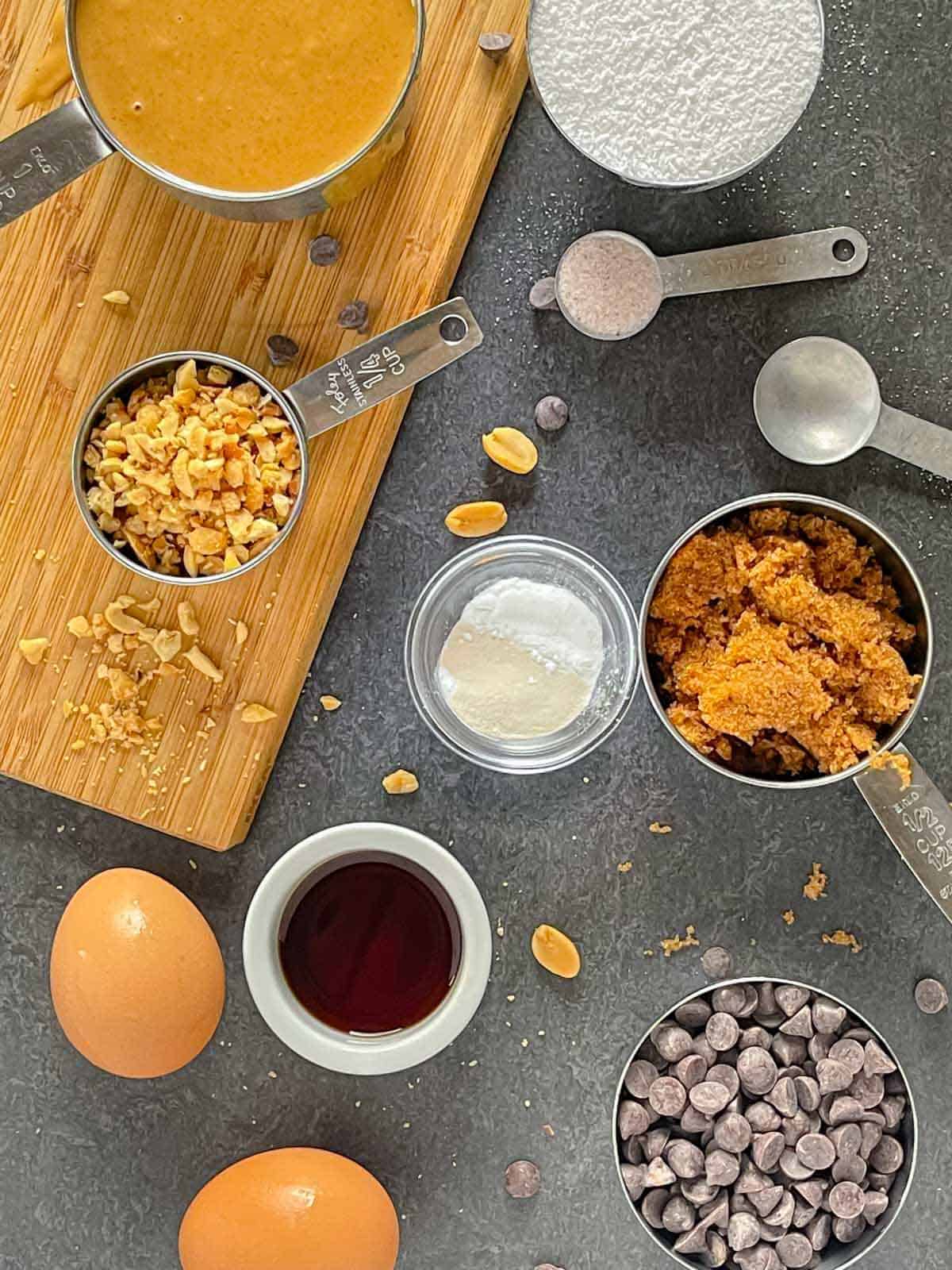 Ingredients for peanut butter cookies in measuring cups and spoons on a grey board.