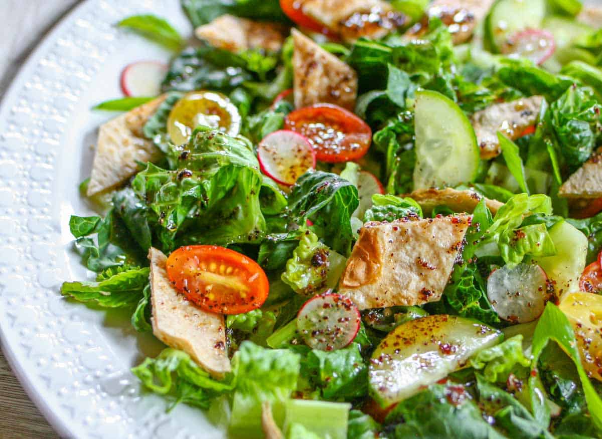 Lebanese fattoush salad on a white plate topped with sumac dressing and crisp tortilla pieces.