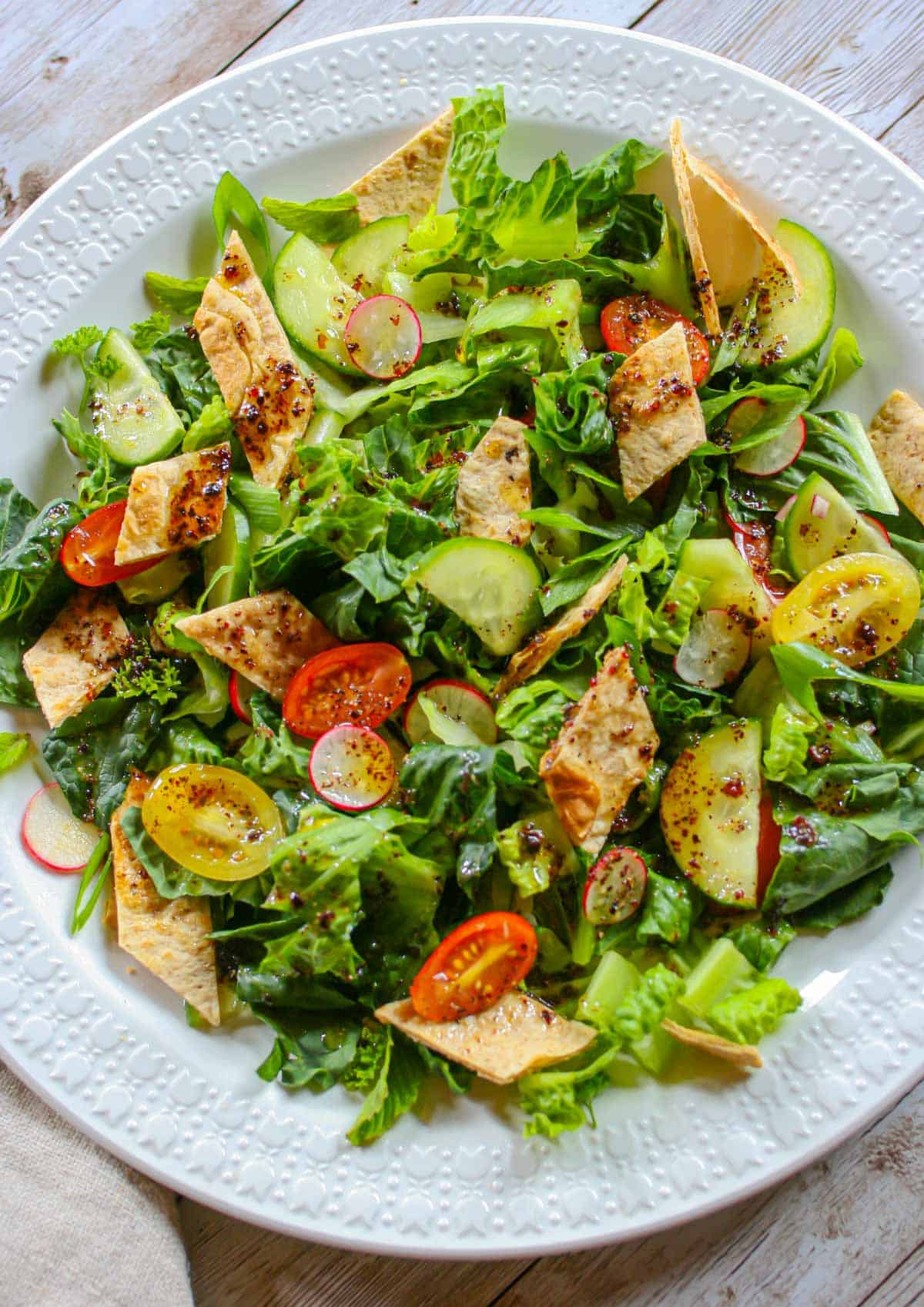 Fattoush salad on a white plate topped with sumac dressing.