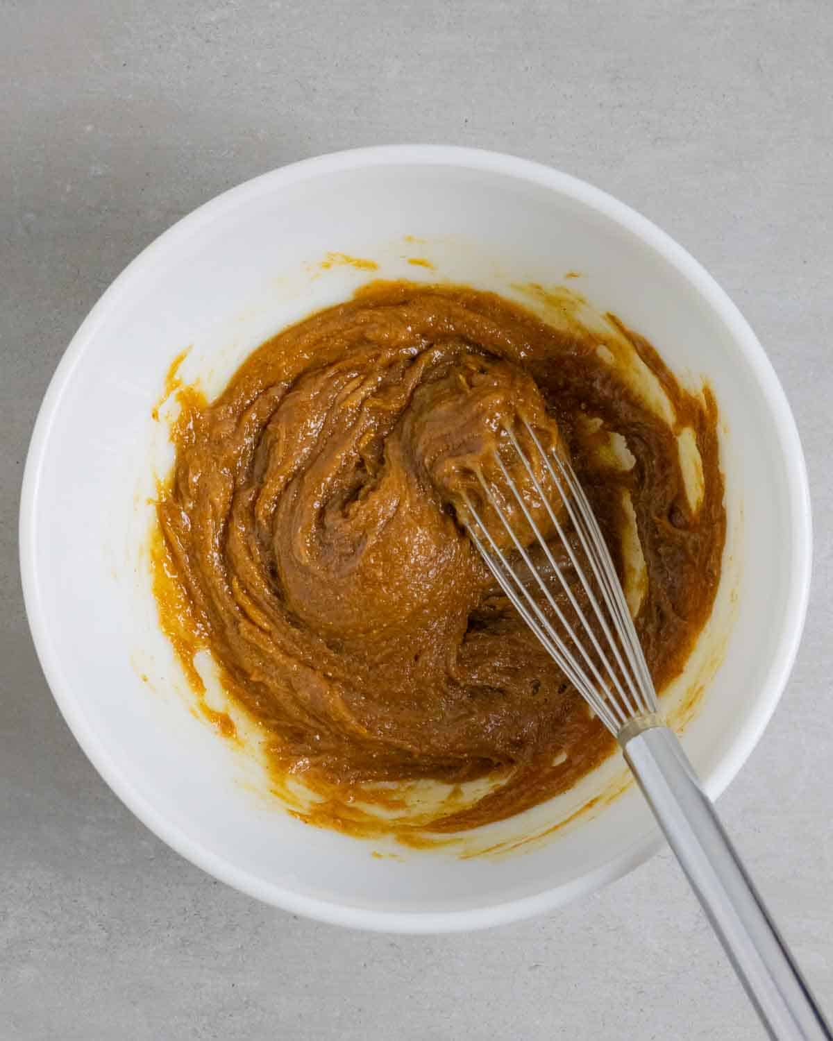 Combined chocolate chip cookie ingredients in a white bowl with a whisk.