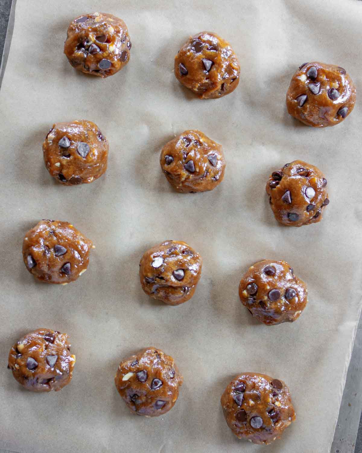 Rolled balls of peanut butter chocolate chip cookie dough on a parchment lined baking sheet.