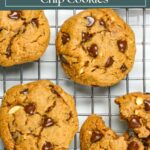 Four peanut butter cookies with chocolate chips on a cooling rack with one broken in half.