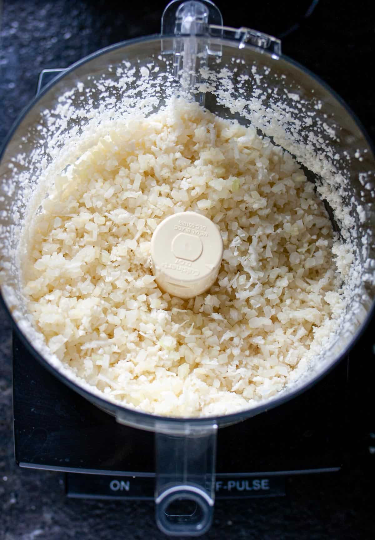 Overhead view of fresh cauliflower in a food processor after it has processed into rice.