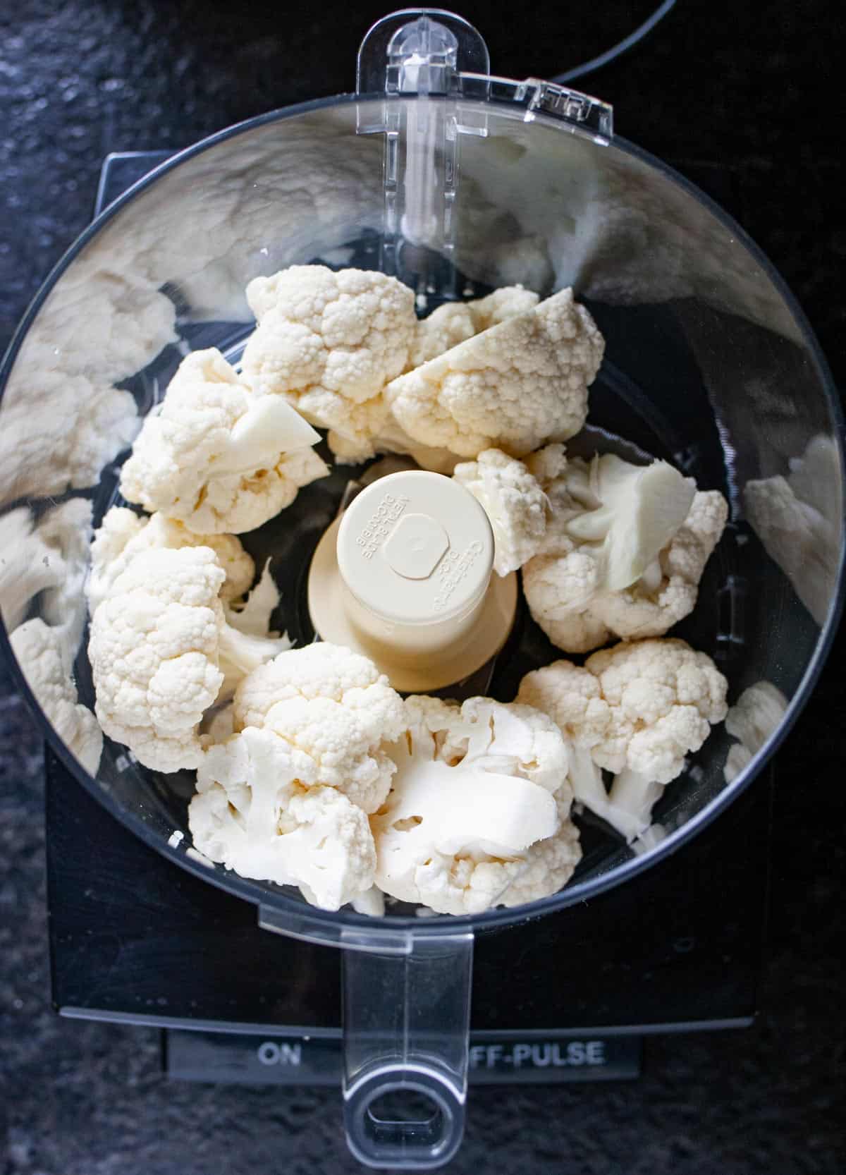 Overhead view of nine fresh cauliflower florets in a food processor ready to process.