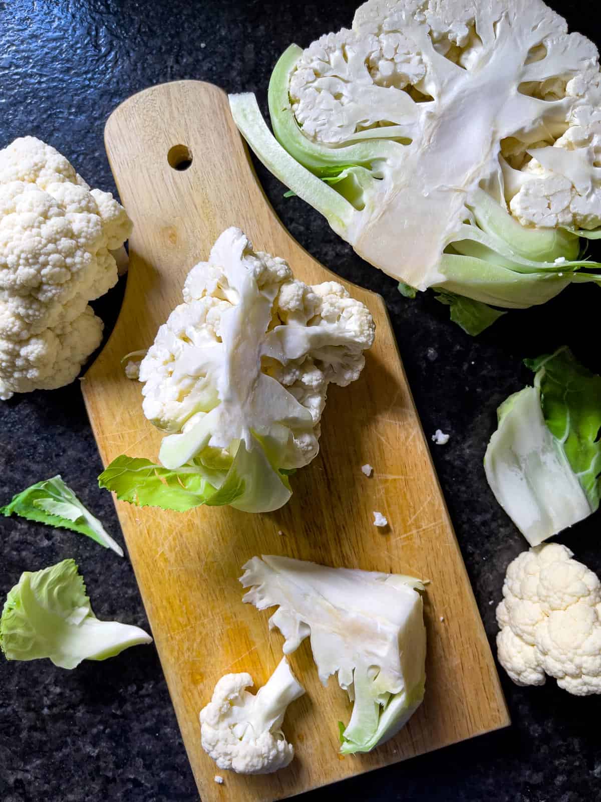 Head of fresh cauliflower cut in half, and another chunk on a hand held cutting board.