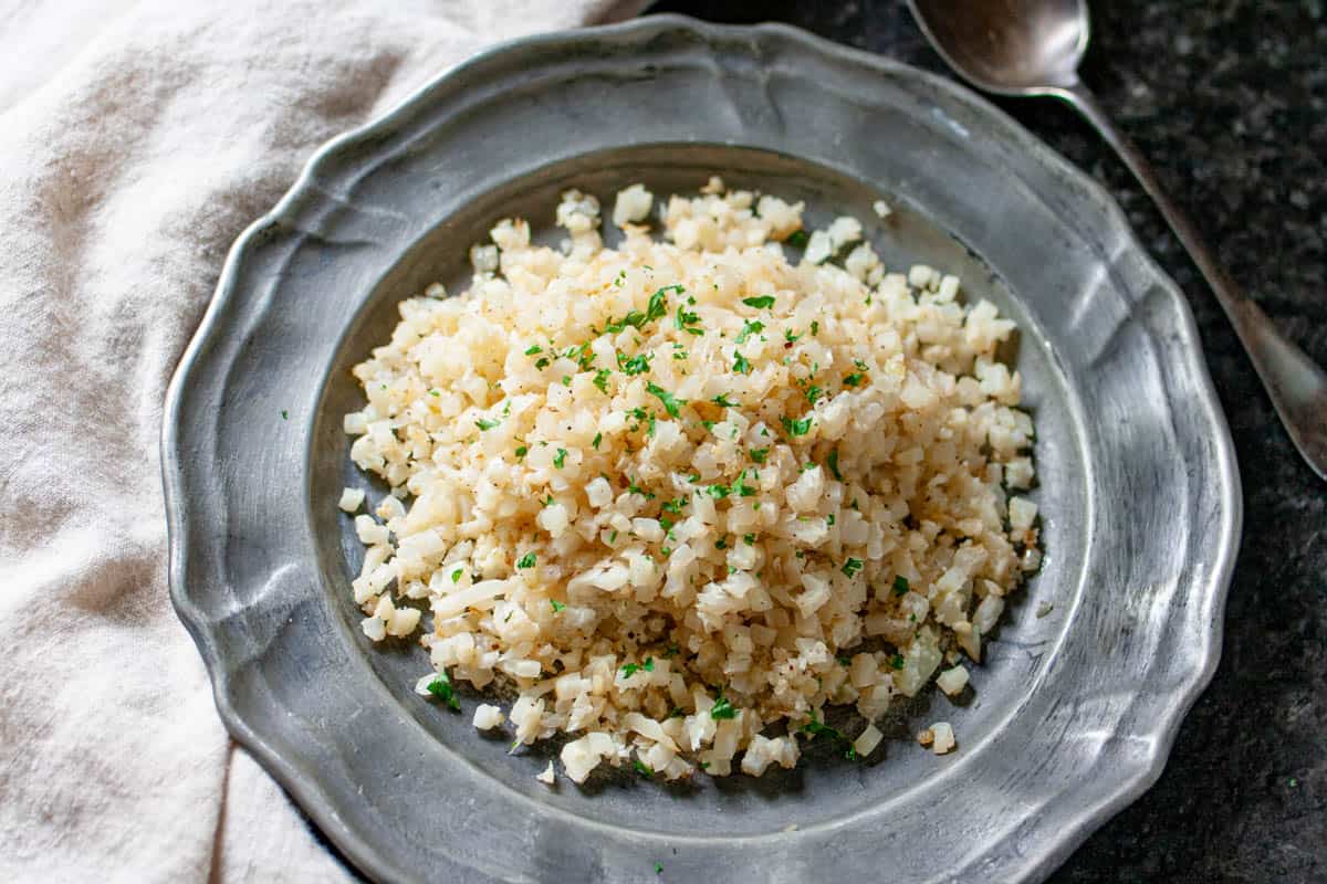 Cooked riced cauliflower on a pewter plate and a sprinkle of parsley on top.