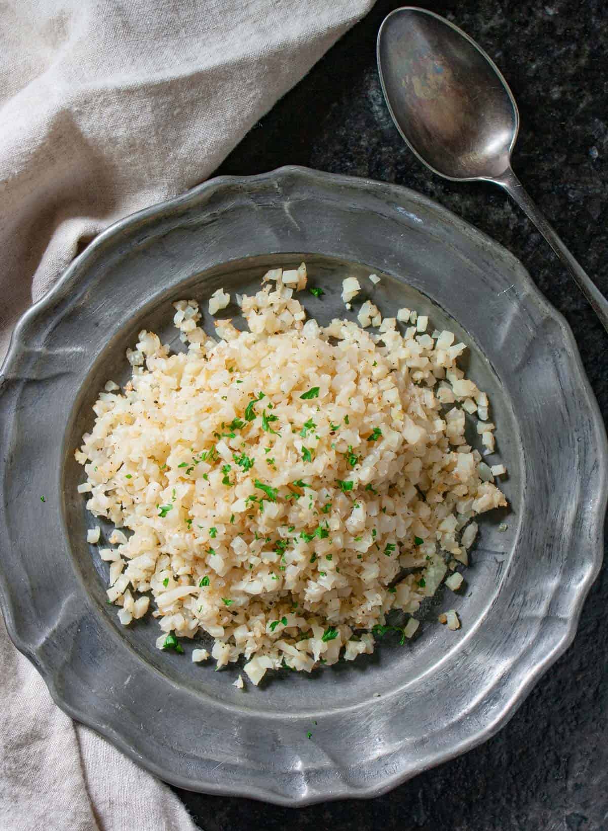 Riced cauliflower on a pewter plate garnished with parsley.