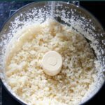 Overhead view of fresh cauliflower in a food processor after it has processed into rice.