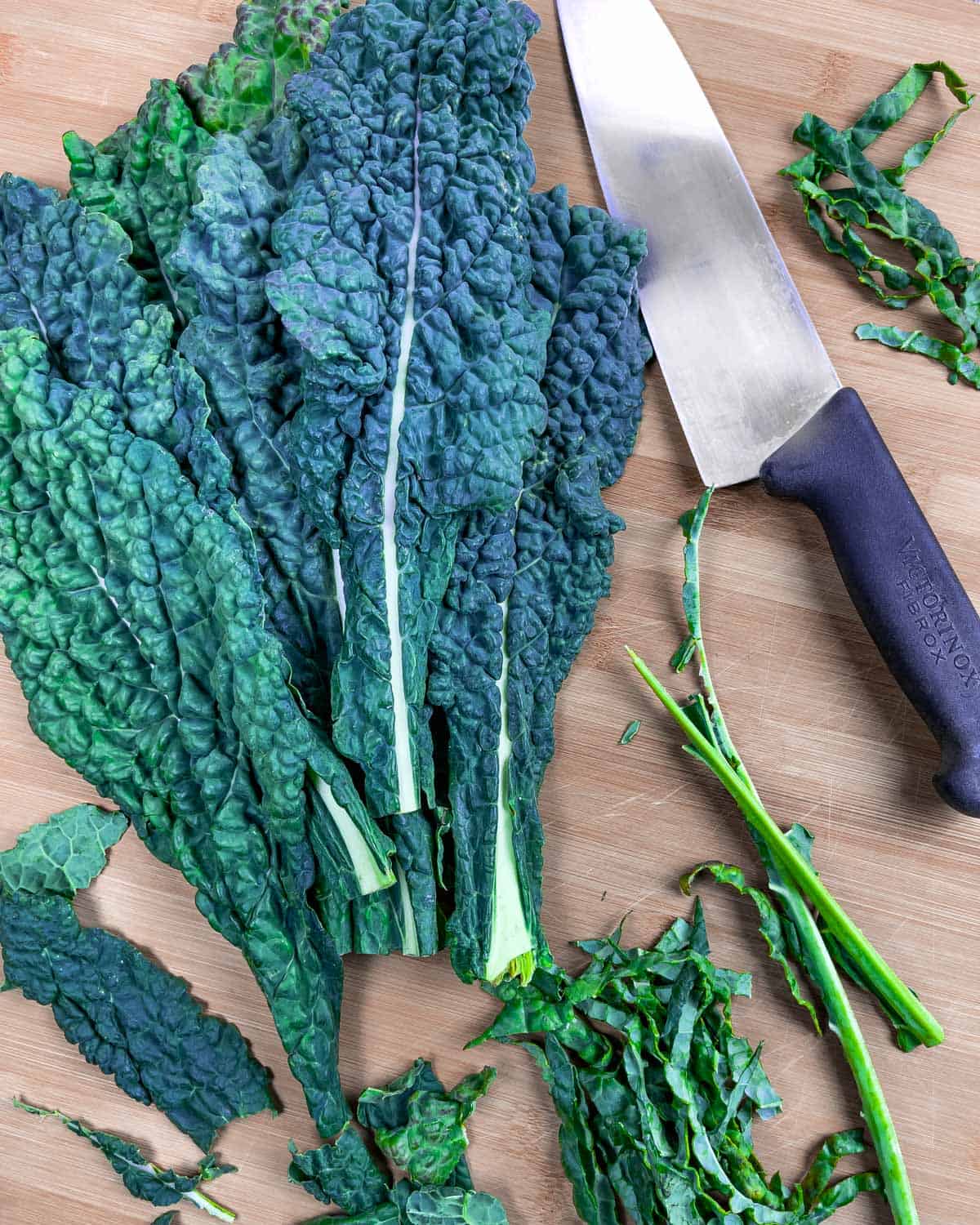 Whole leaves of kale on a cutting board with a knife, showing some destemmed and chopped.