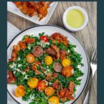 Cavolo nero kale BLT salad in a white plate on a wood board with a fork on the side.