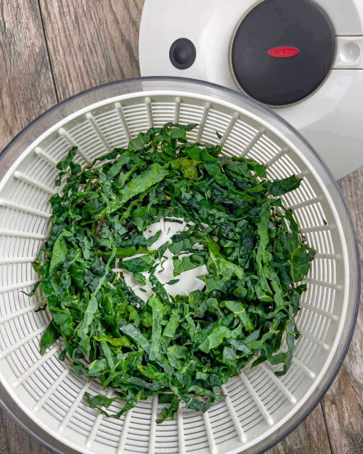 Shredded kale in the basket of a salad spinner with lid next to it.