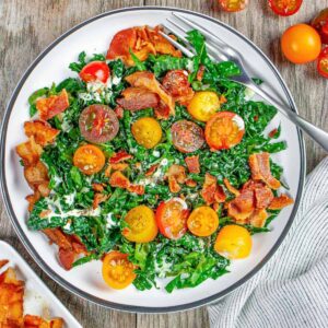 Cavolo nero kale BLT salad in a white plate on a wood board with a fork on the side.