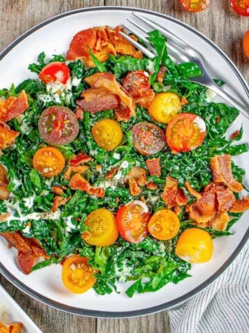 Cavolo nero kale BLT salad in a white plate on a wood board with a fork on the side.