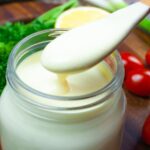 Mason jar of lemon dressing with small wooden spoonful of dressing dripping back into the jar.