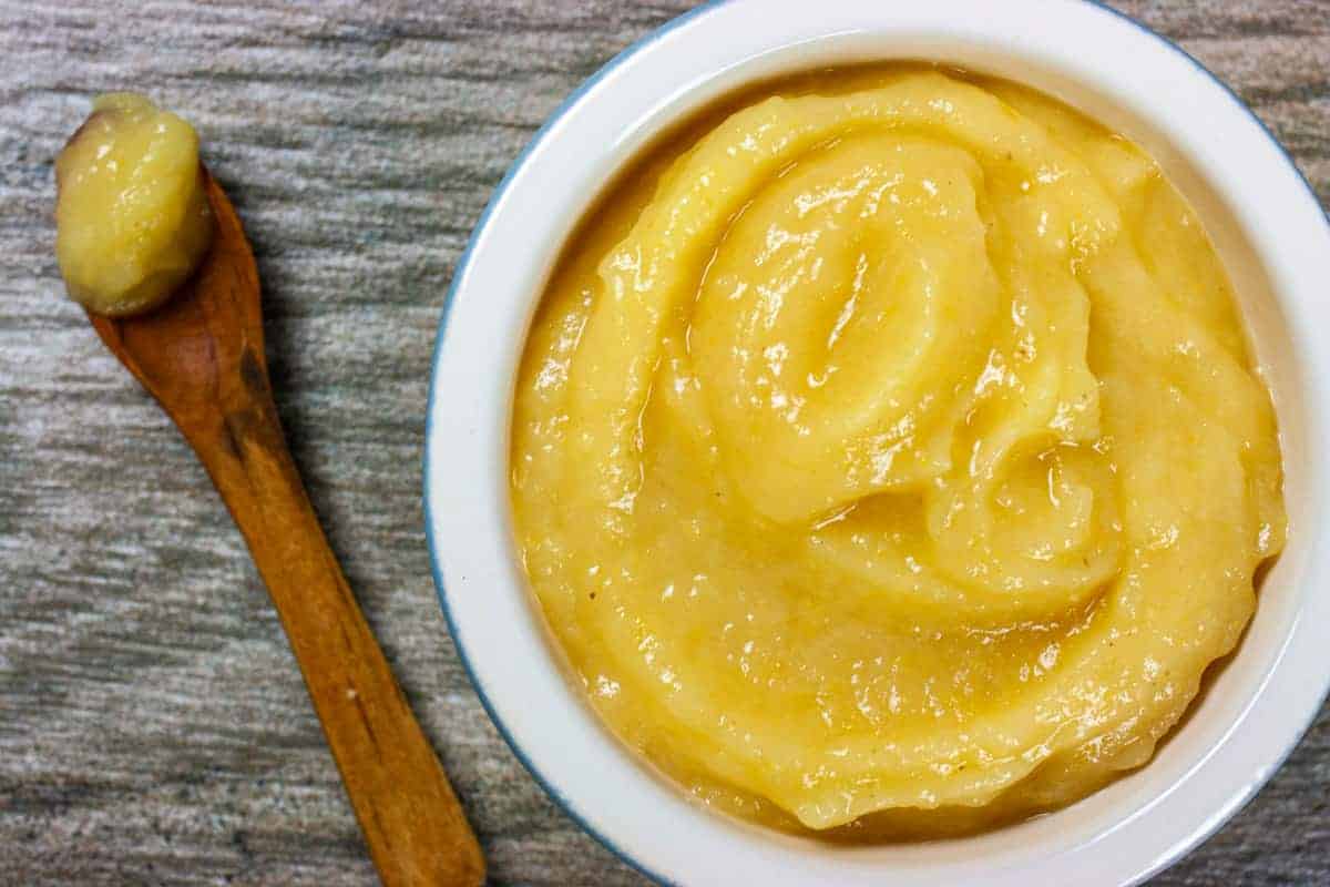 Overhead view of bright yellow lemon puree in a ramekin on a grey wood background with a wooden spoon with puree next to the ramekin.