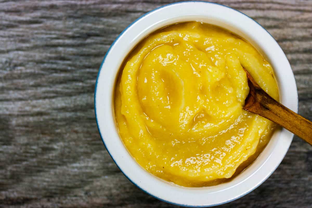 Overhead view of bright yellow lemon puree in a ramekin with a wooden spoon in it. 
