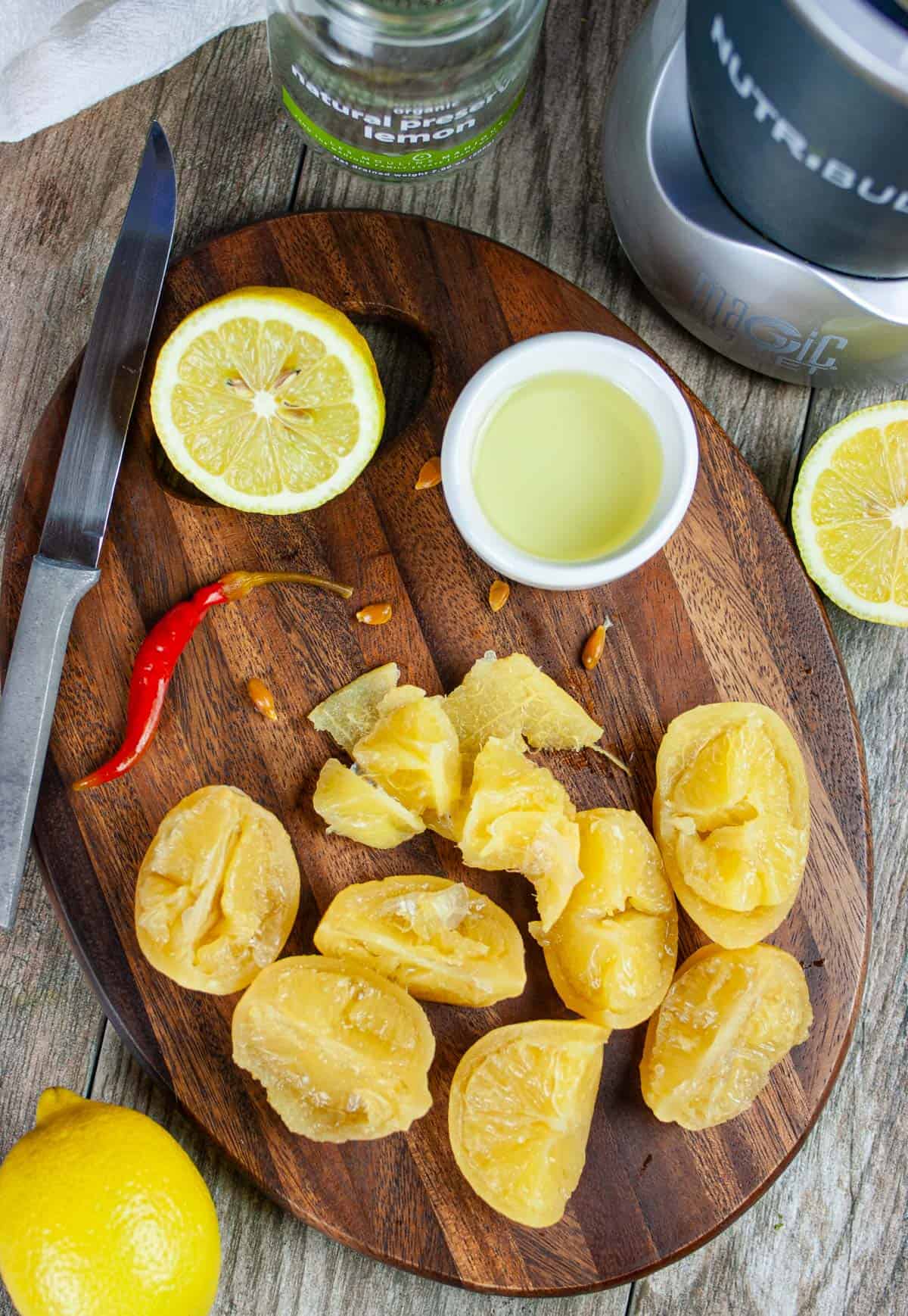 Sliced preserved lemons on a cutting board with juice in a small ramekin and a red pepper from the jar.