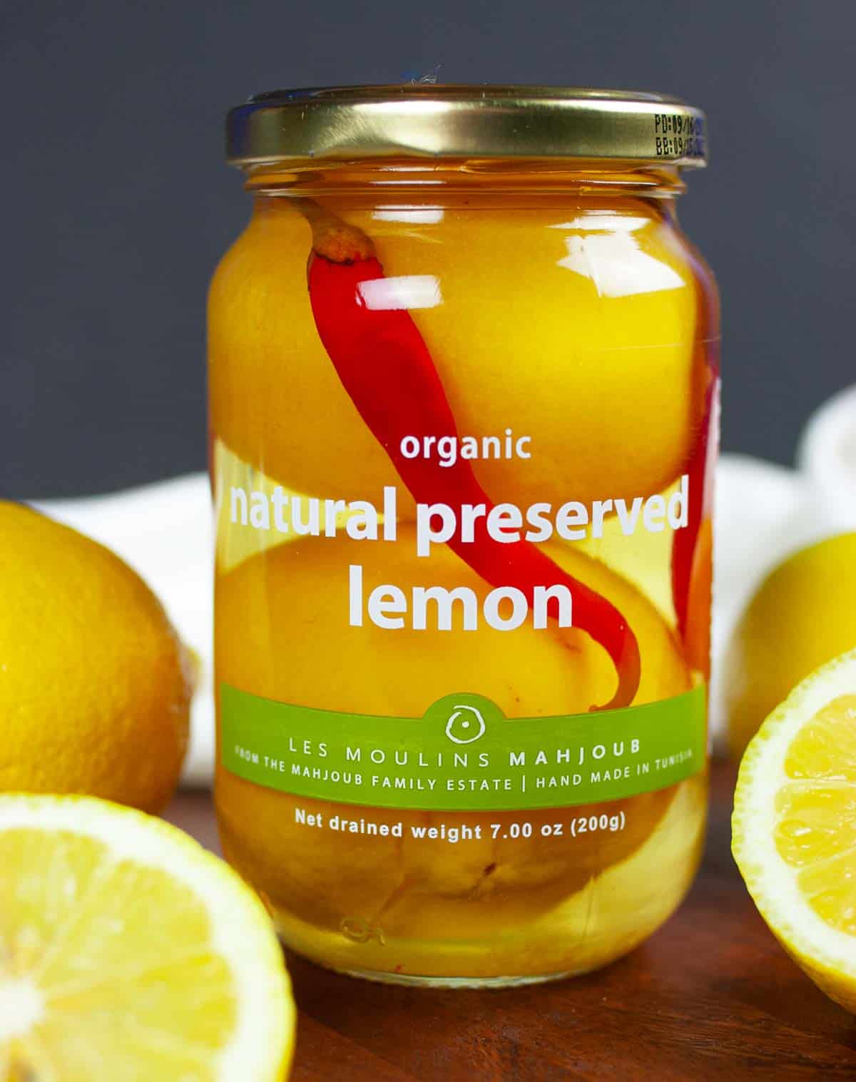 Unopened jar of organic preserved lemon on a cutting board with sliced lemons surrounding it.