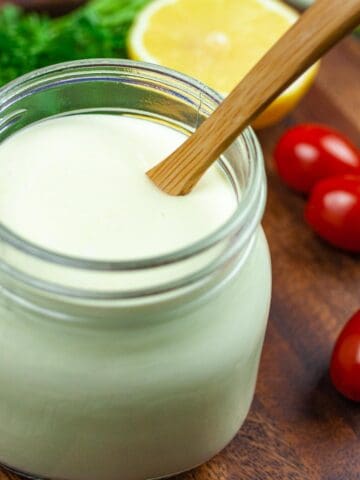 Small mason jar of lemon dressing with small wooden spoon of dressing dripping back into the jar.