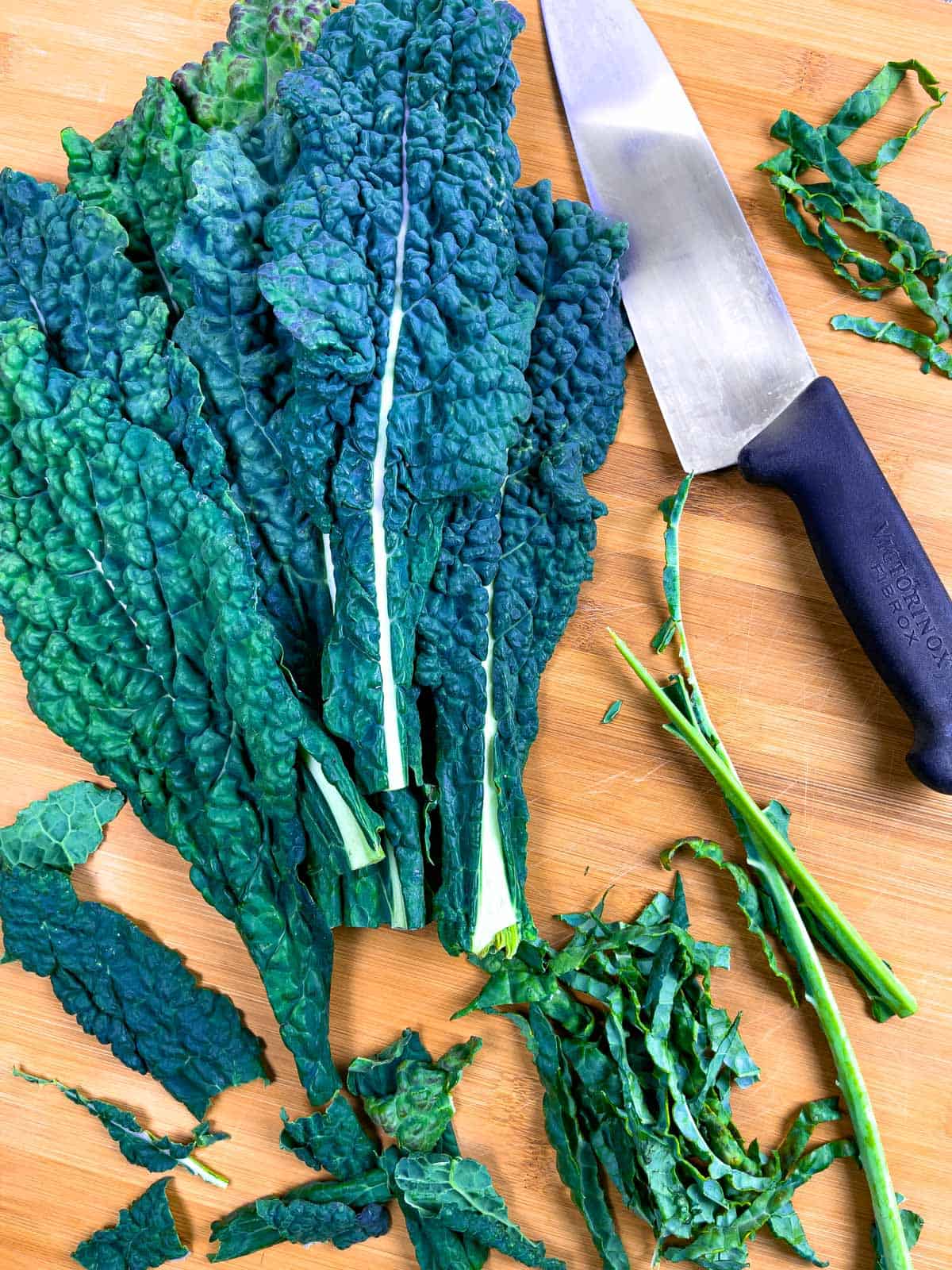 Whole leaves of kale on a cutting board with a knife, showing some destemmed and chopped.