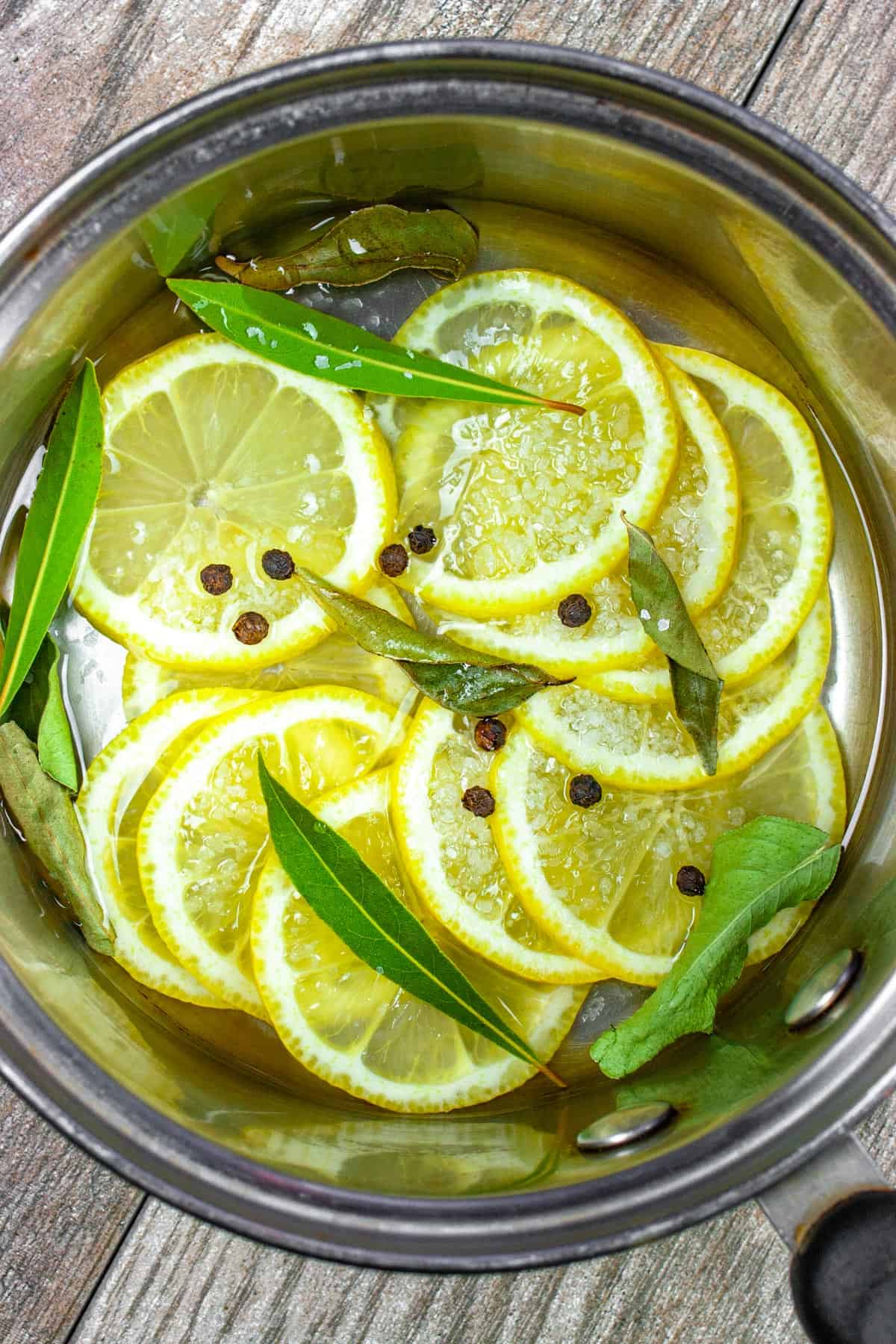 Sliced fresh lemons in a sauce pan with water, salt, peppercorns and spices. 
