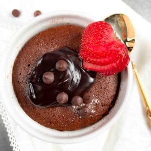 Top down view of a mug cake in a ramekin with chocolate sauce, chips, and a sliced strawberry.