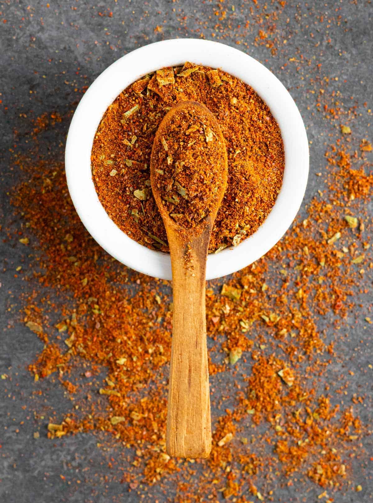 Low-fodmap taco seasoning in a white bowl with a small wooden spoon.