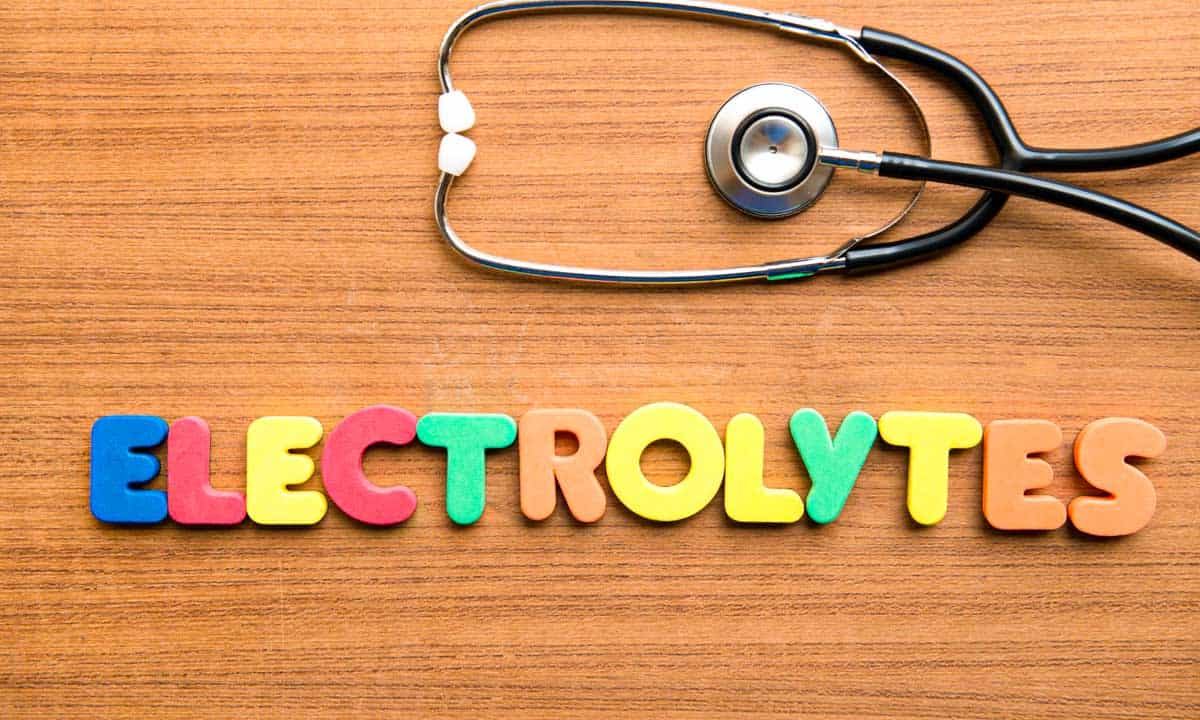 Electrolytes, spelled out in multi-colored kids toy letters on a wood grained background with a stethoscope laying above it.