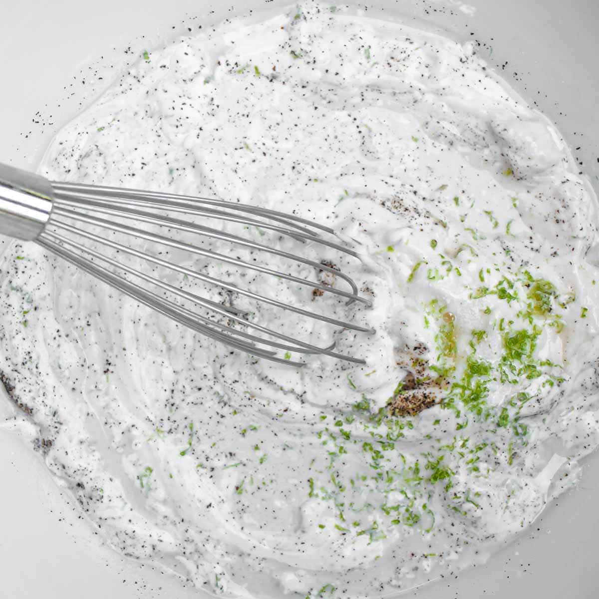 Gluten-free coleslaw dressing in a white bowl with a whisk.