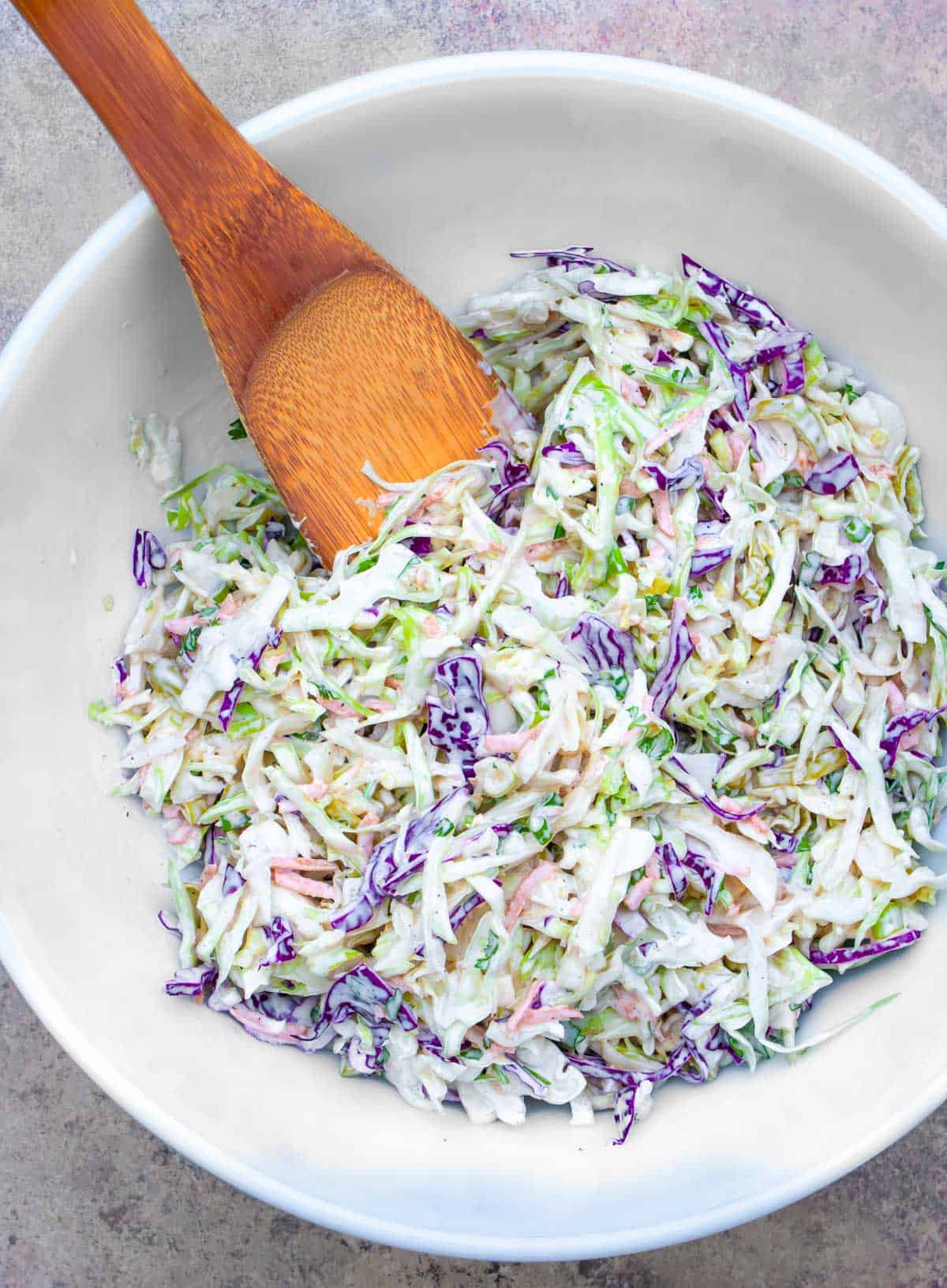 Dairy-free coleslaw mixed in a white bowl, with a wooden spoon.