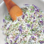 Dairy-free coleslaw mixed in a white bowl, with a wooden spoon.