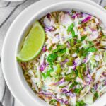 Cilantro lime coleslaw in a white bowl with a lime and cilantro garnish.