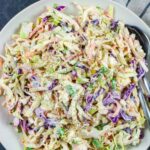 Keto coleslaw seasoned with pepper in a white bowl with a fork and spoon.