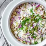 White bowl of dairy-free creamy coleslaw topped with chopped cilantro and pumpkin seeds.