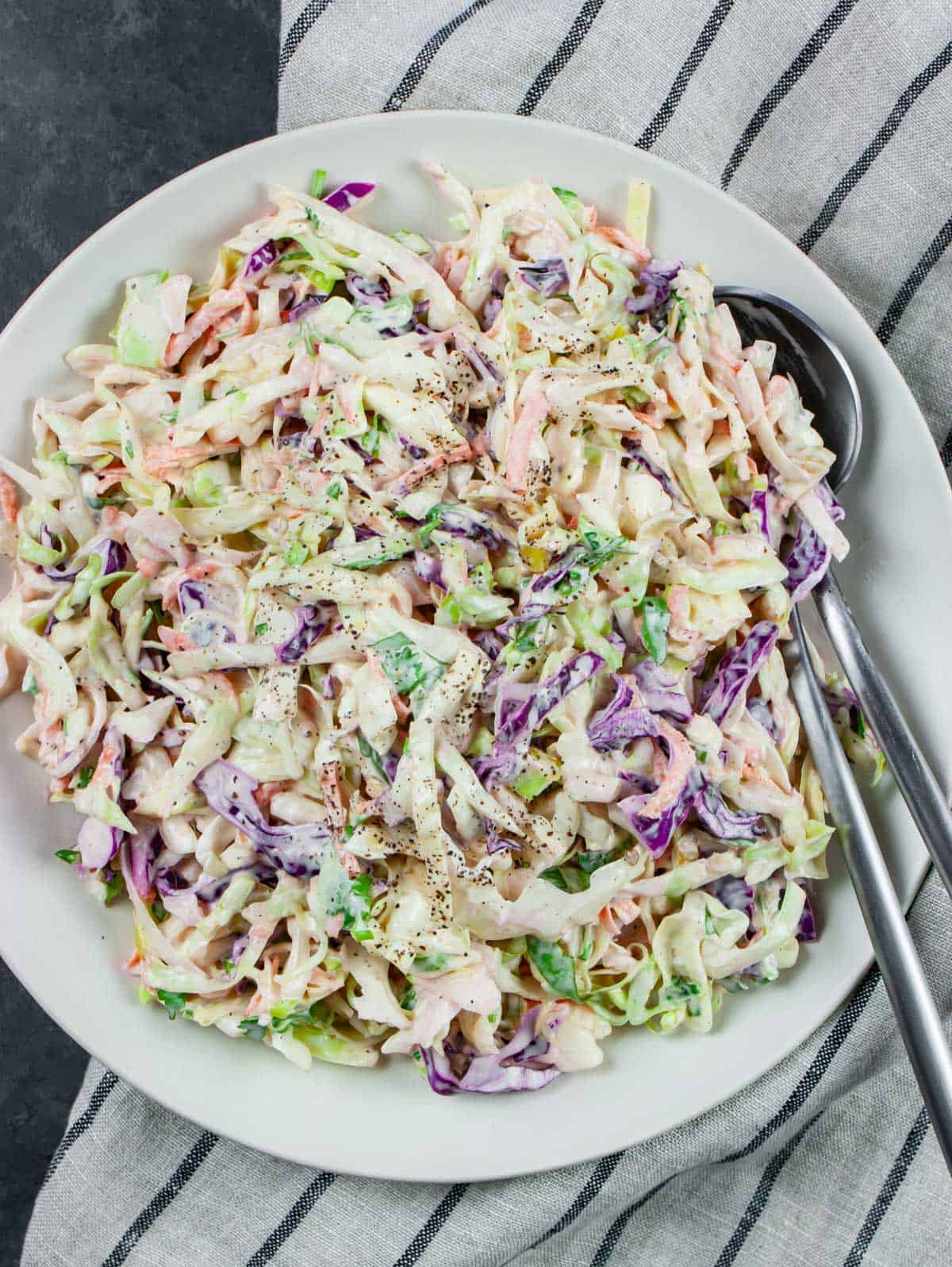 keto coleslaw seasoned with pepper in a white bowl with a fork and spoon.