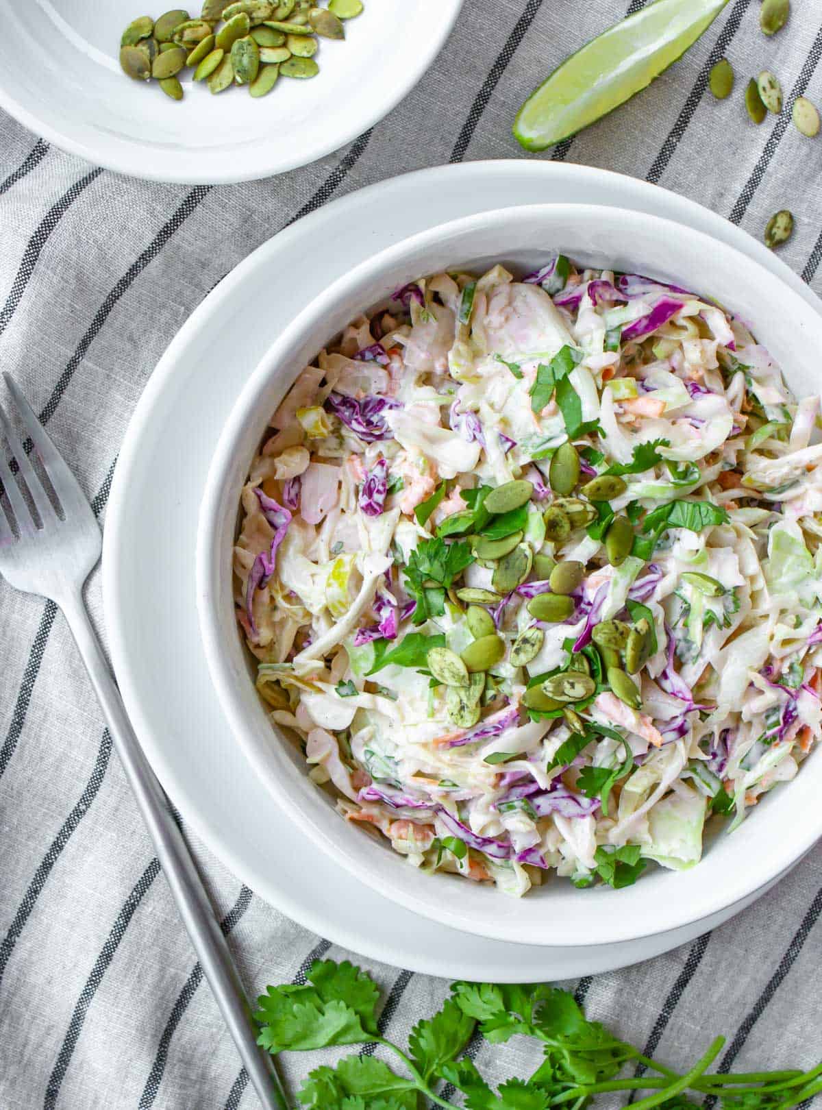 White bowl of dairy-free creamy coleslaw topped with chopped cilantro and pumpkin seeds.