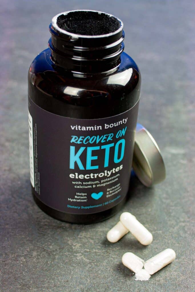 Open bottle of keto electrolyte capsules with a few caps in front of the bottle.