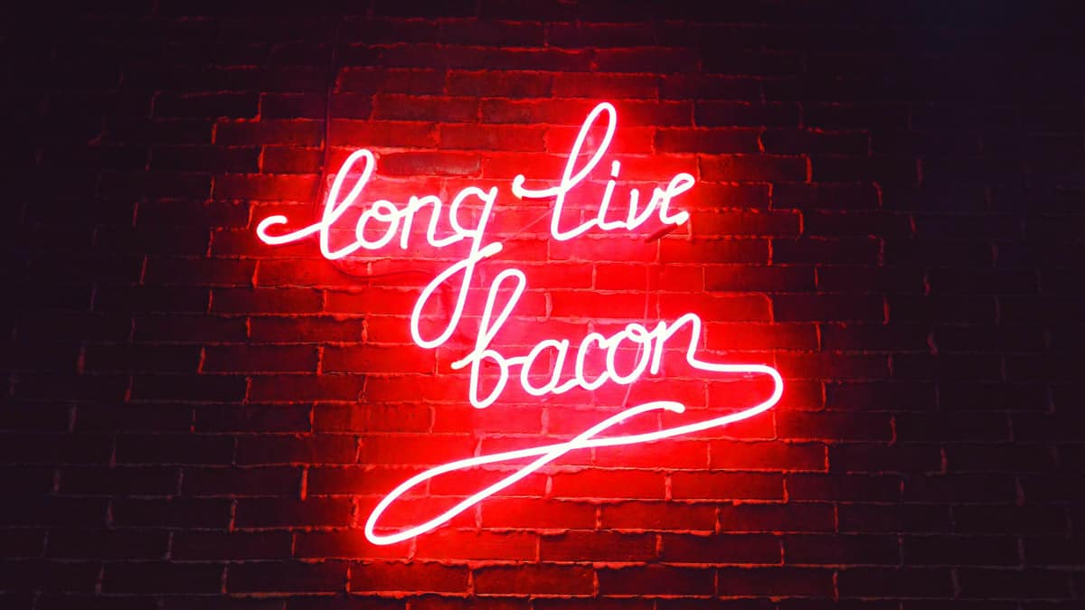 Brick wall with red neon cursive sign saying long live bacon.