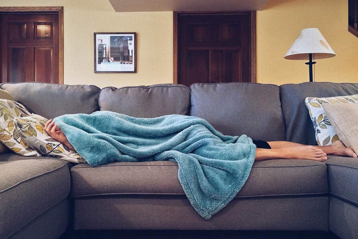 Person laying on a couch under a blue blanket.
