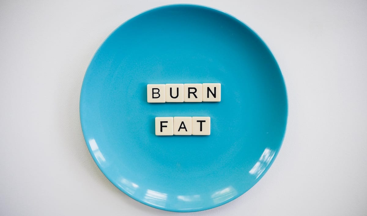 Scrabble letters on a blue plate that spell Burn Fat.