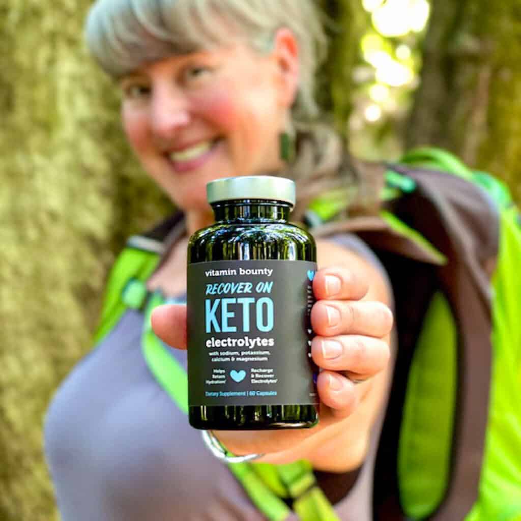 Blog author wearing a backpack holding a bottle of vitamin bounty keto electrolyte capsules.