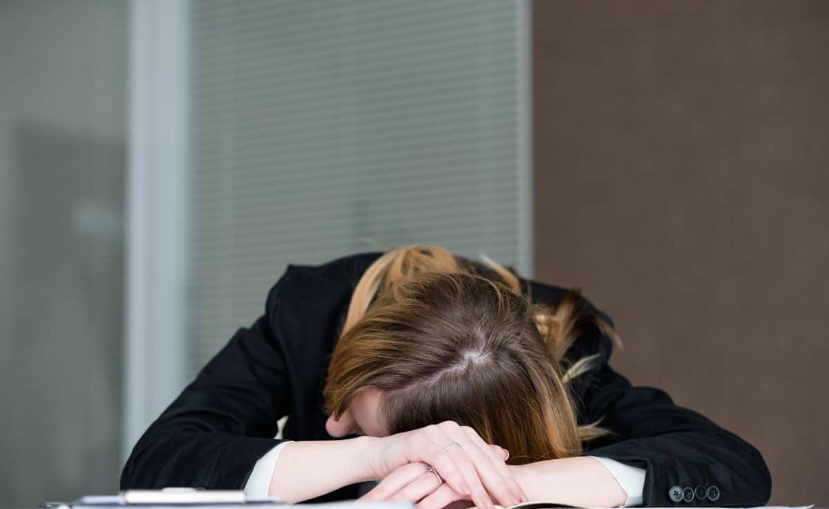 Sitting tired woman in a black coat with her head down on her arms on a table.