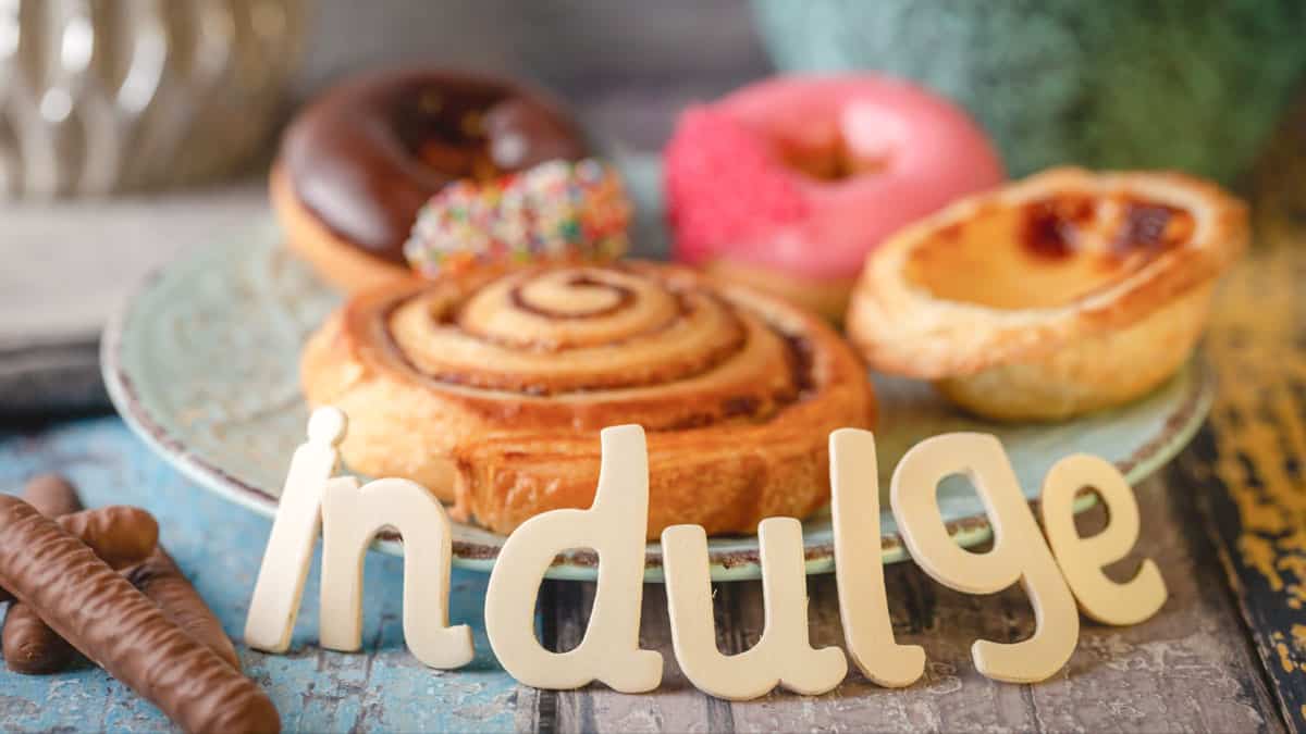 Cinnamon roll and doughnuts on a plate with the word indulge in front.