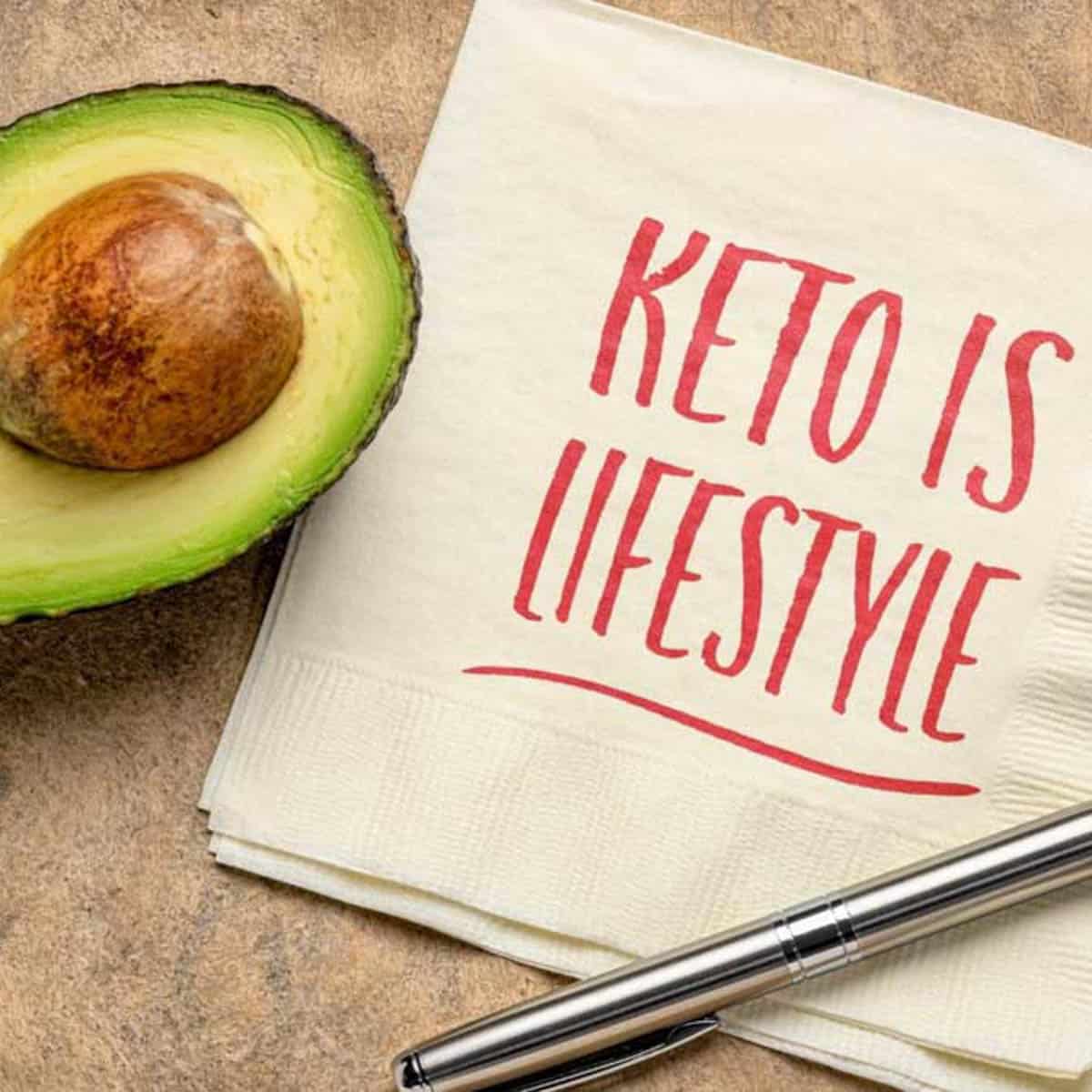Keto Is Lifestyle in red ink on a square napkin with half an avocado next to it.